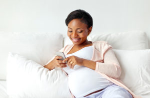 pregnancy, people and technology concept - happy pregnant african american woman with smartphone in bed at home