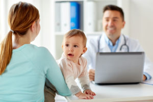 medicine, healthcare, pediatry and people concept - happy woman with baby and doctor with laptop computer at clinic