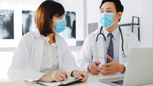 Medical team of asia serious male and young female doctor with protective face masks discussing computed tomography result in hospital office. Social distance, Lifestyle new normal after corona virus.