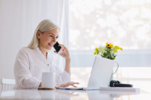 Woman talking on the phone, using laptop. Working from home, freelancing, online job.