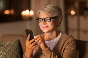 technology, communication and people concept - happy senior woman in glasses with smartphone at home in evening