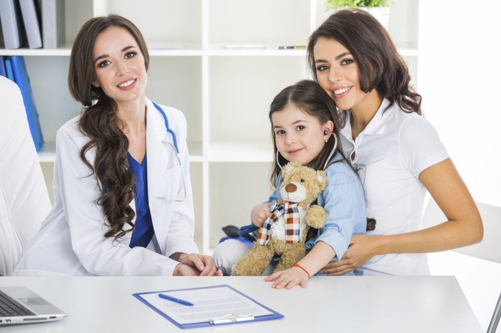 Happy mother and child with teddy bear and stethoscope at pediatrician office